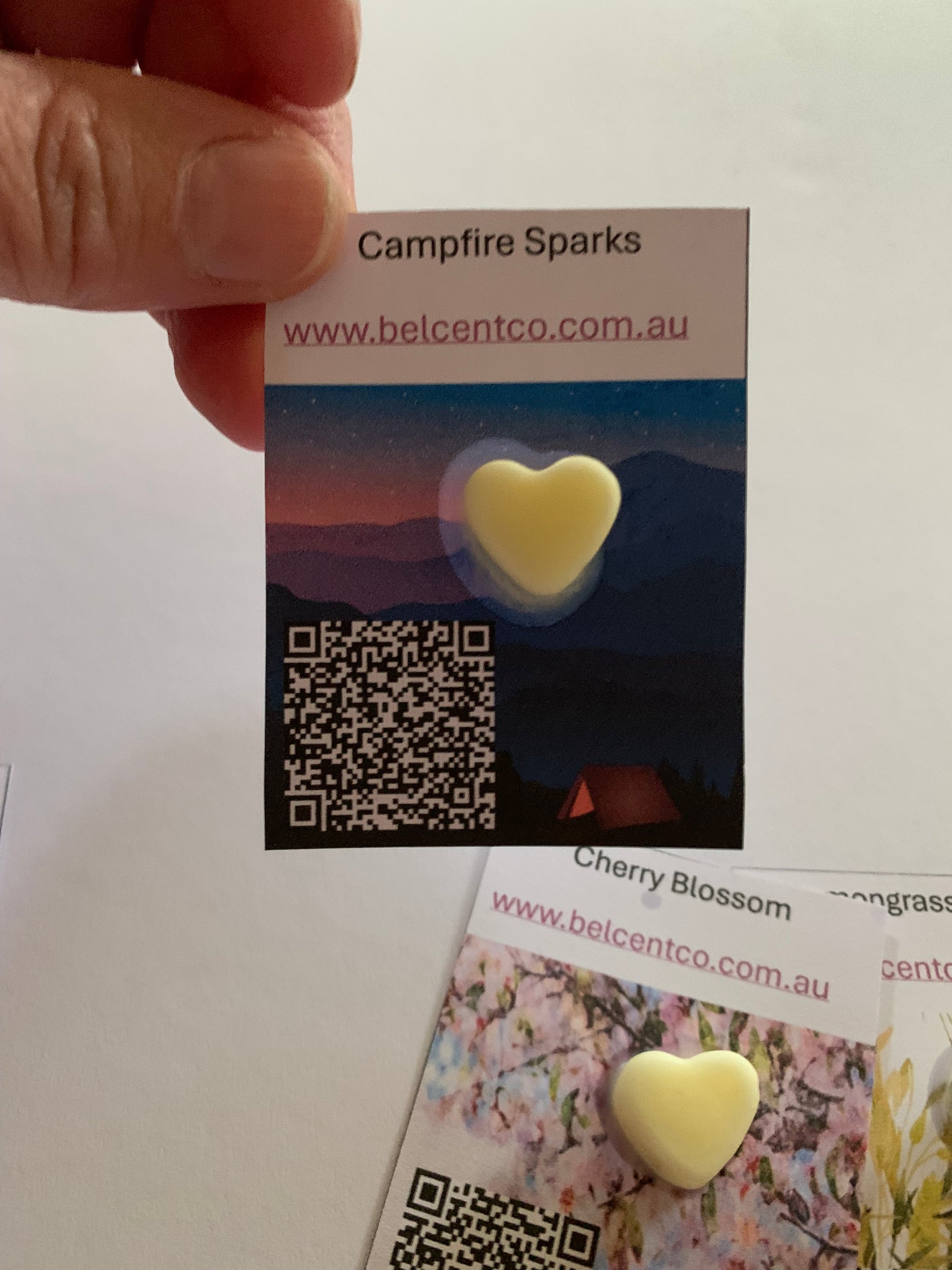 Heart-shaped object with a QR code on a label held by a hand, with a magazine in the background.