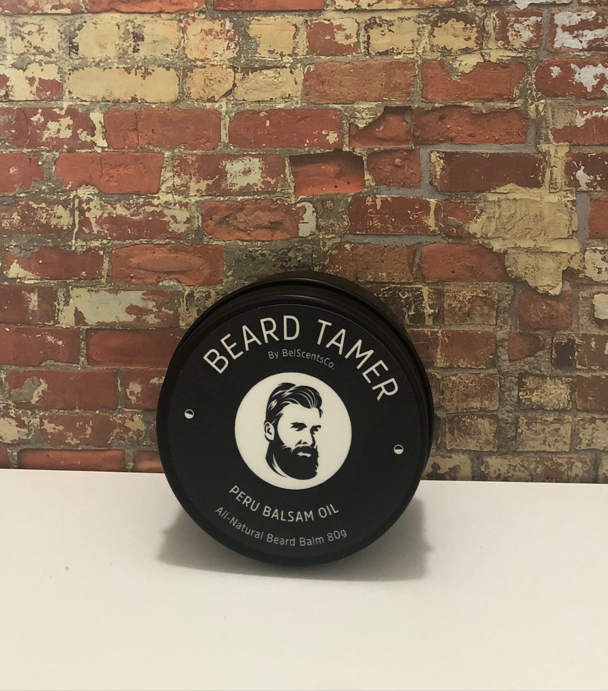 All-Natural Beard Balm for Men in Tin Container – Conditioning and Styling Balm with Essential Oils for Soft, Healthy Beard Care. Scented in Peru of Balsam Oil displayed on industrial brick wall setting