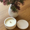 White smooth candle round set against oak table and white vase with Australian bush botanicals 