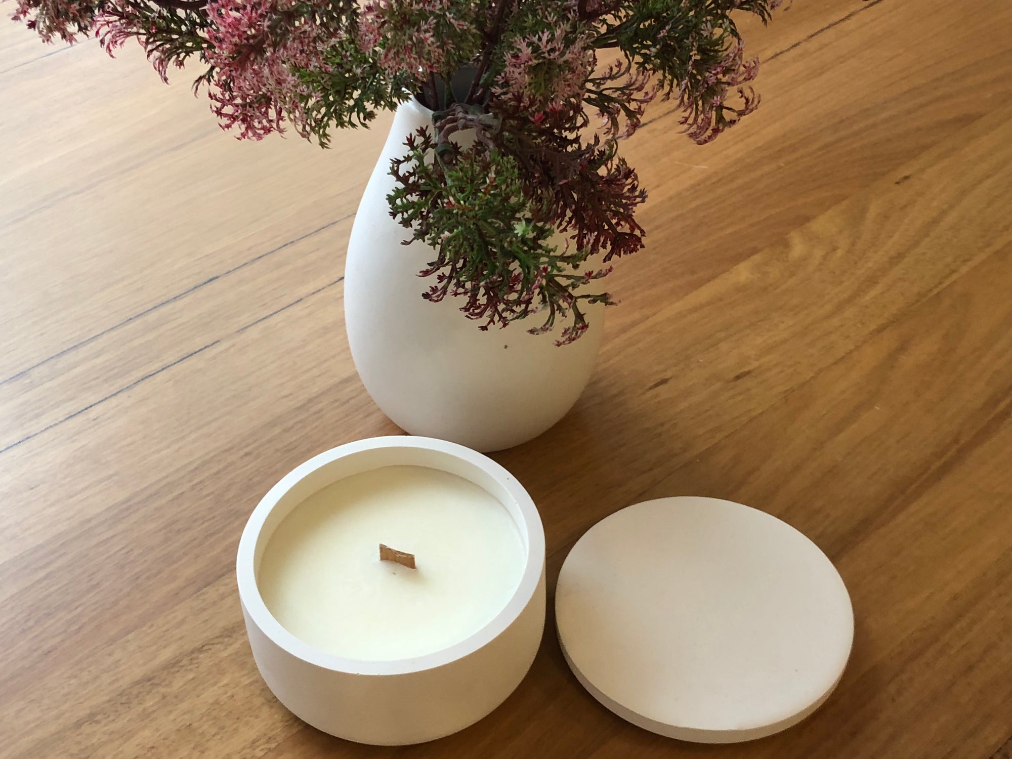White smooth candle round set against oak table and white vase with Australian bush botanicals 