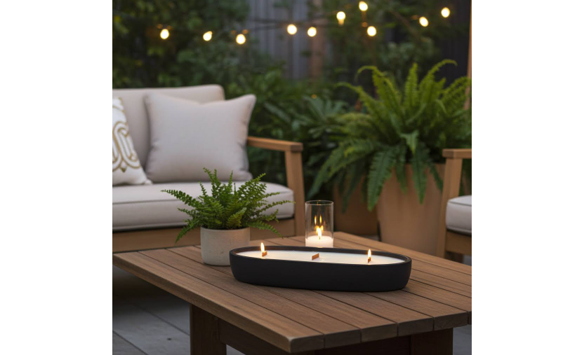Black Candle Oval Shaped placed on outdoor coffee table, evening setting with Fenton lighting in the background