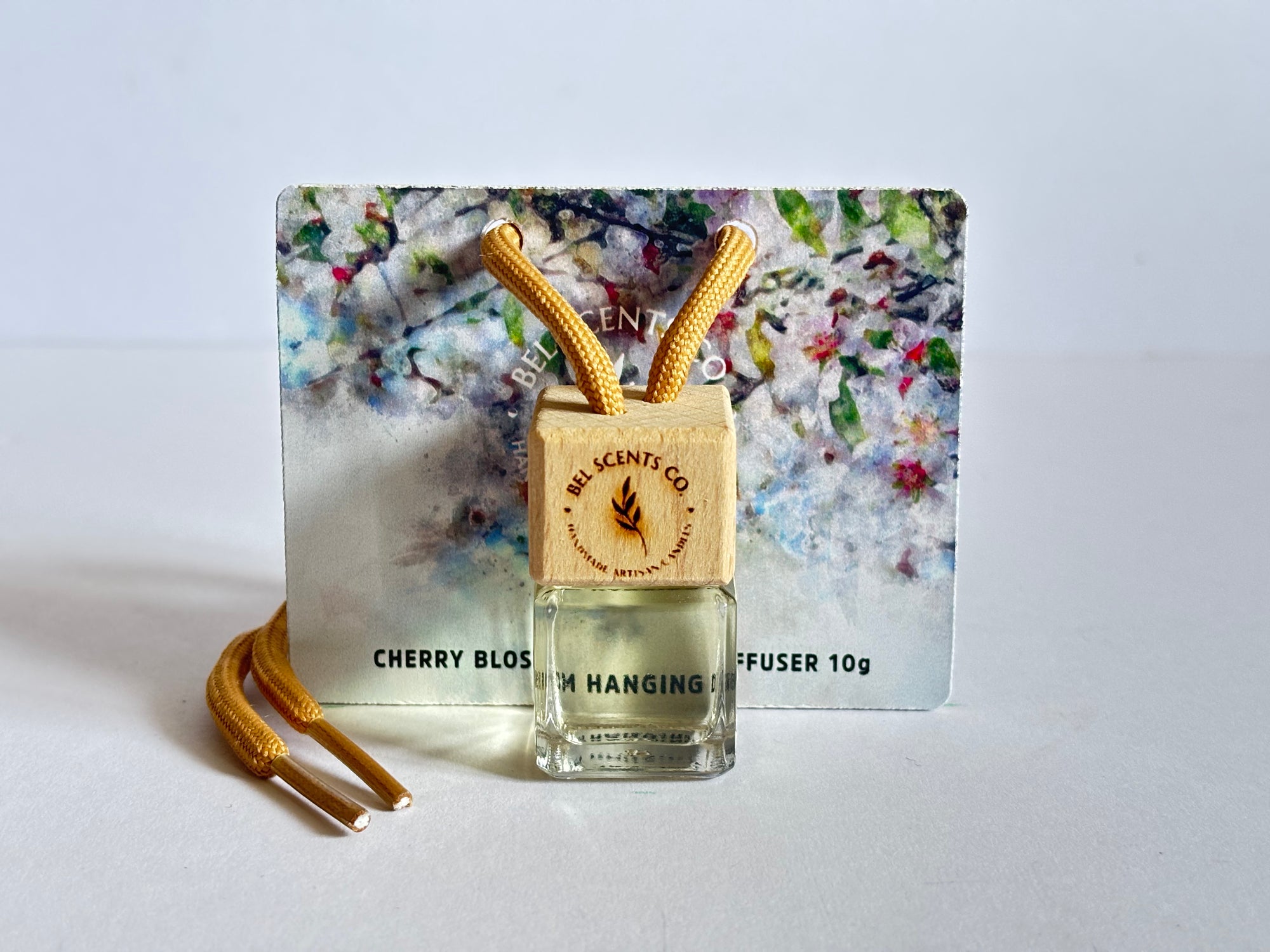 Cherry Blossom Scented hanging car diffuser bottle with wooden cap, suspended by string. Minimalist hanging diffuser for car interior. Hanging fragrance diffuser with Wood-topped diffuser adding a refreshing scent to a car interior. filled with essential oils for natural fragrance