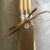 Set of four beige candles tied with brown string and a tag on a neutral background