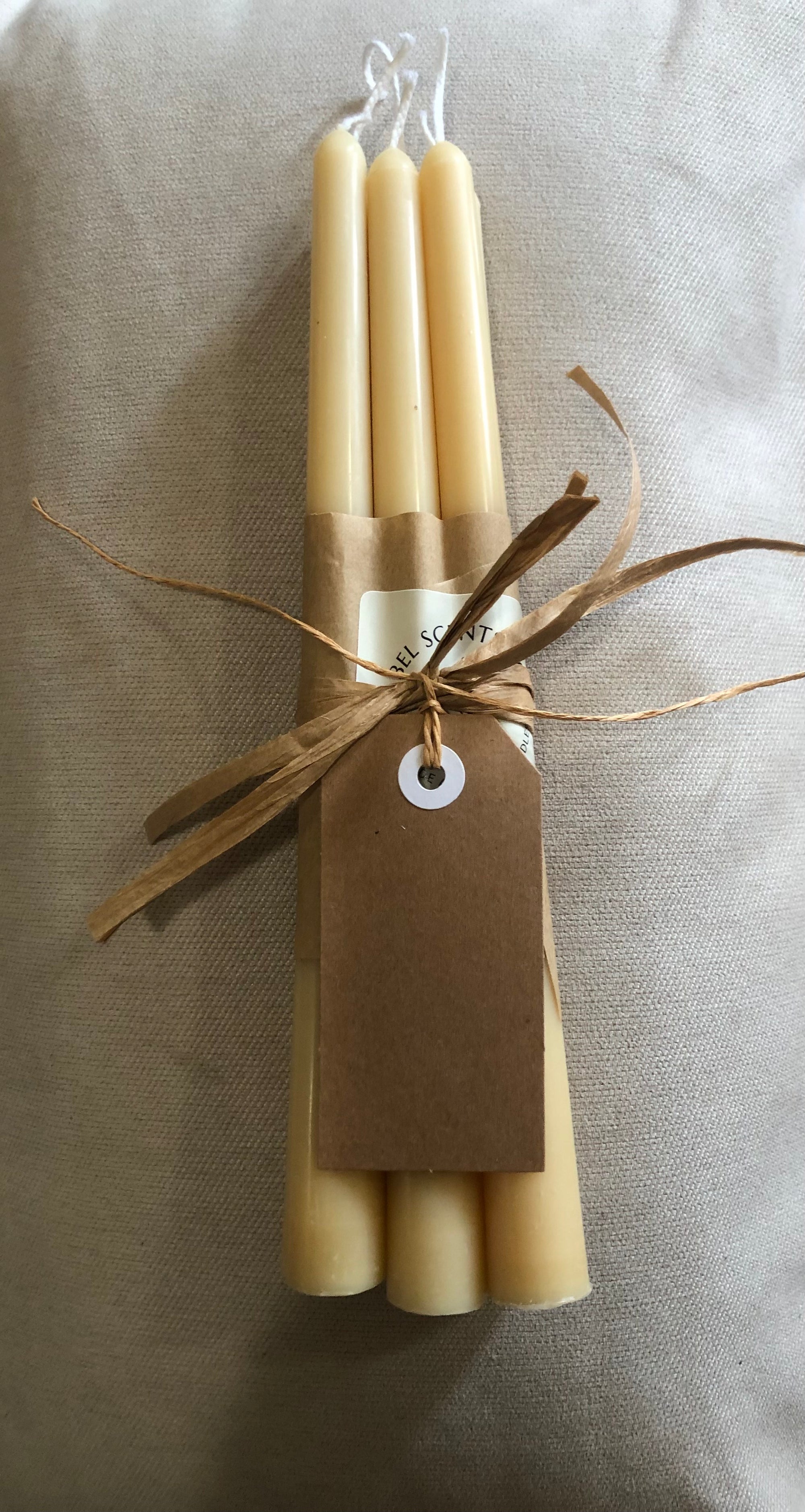 Set of four beige candles tied with brown string and a tag on a neutral background
