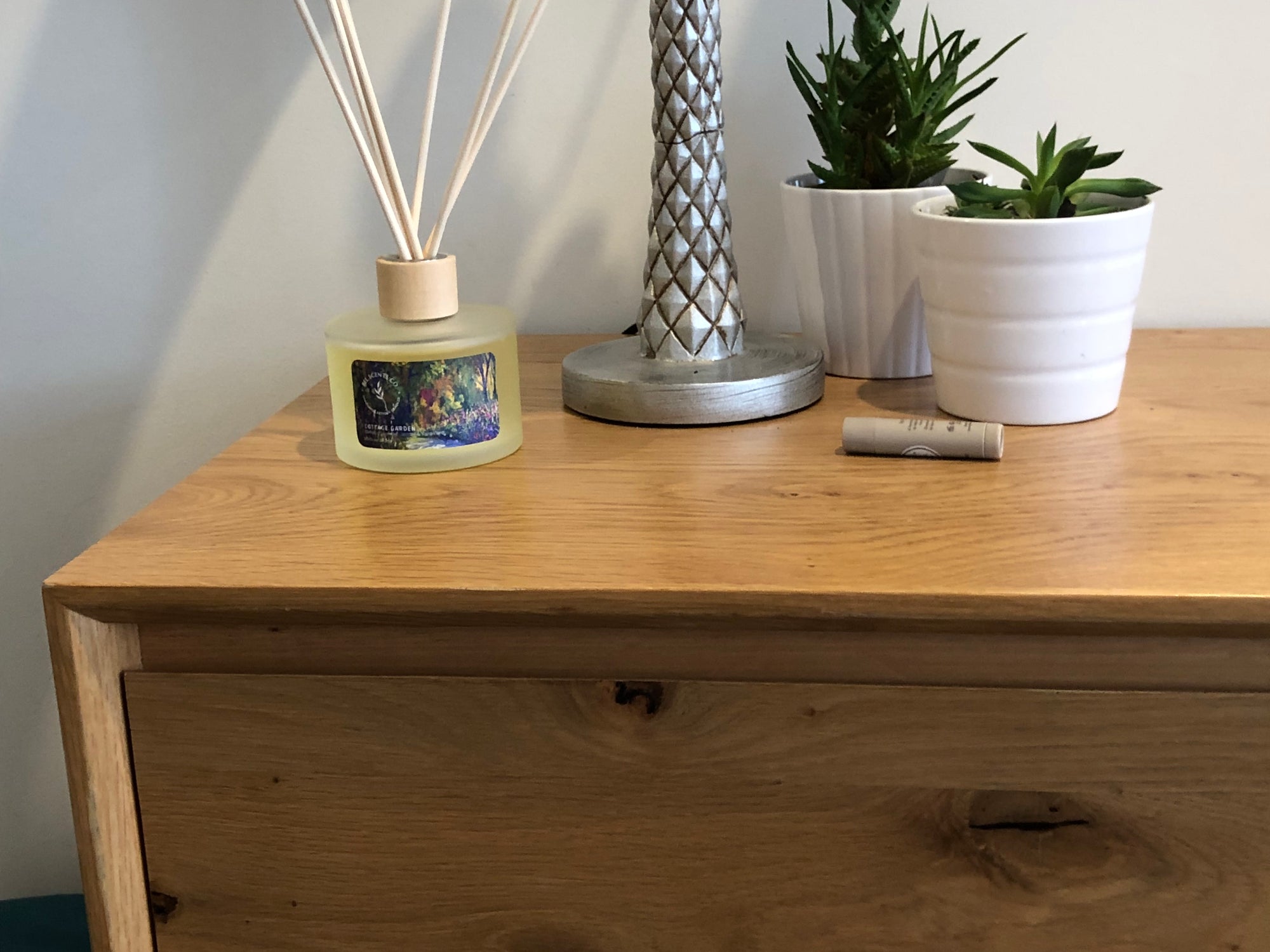 Reed Diffuser with wooden cap and frosted glass placed on wooden cabinet. 